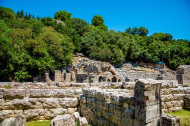 Arnavutluk 'un Butrint kentindeki antik taş duvarlar yemyeşil yapraklar arasında yükselerek, katmanlı Yunan ve Roma etkilerine sahip bir UNESCO miras alanını ortaya çıkardı