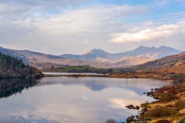 Snowdonias Llyn Gwynant reflects a majestic mountain panorama under a vibrant Welsh sky, capturing serene beauty in North Wales.