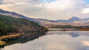 Snowdonias Llyn Gwynant reflects a majestic mountain panorama under a vibrant Welsh sky, capturing serene beauty in North Wales.