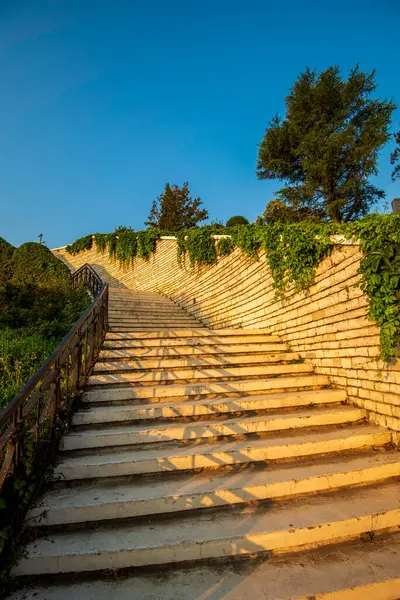 Permets stone steps rise under a warm sunset glow, framed by climbing vines and revealing a tranquil Albanian hillside vantage