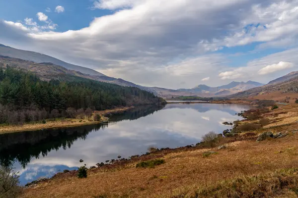 Snowdonias Llyn Gwynant reflects a majestic mountain panorama under a vibrant Welsh sky, capturing serene beauty in North Wales.