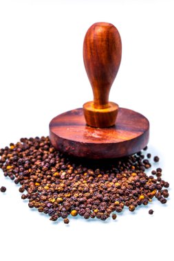 Closeup of a handcrafted wooden tamper resting on scattered black peppercorns against a white backdrop