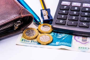 İngiliz finansal araçlarının makro çekimi, içinde deri cüzdan, sterling bozukluklar, beş poundluk banknot, hesap makinesi anahtarları, metalik kalem ve mavi bileyici var.