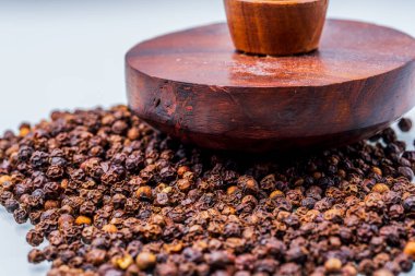 Closeup of a handcrafted wooden tamper resting on scattered black peppercorns against a white backdrop