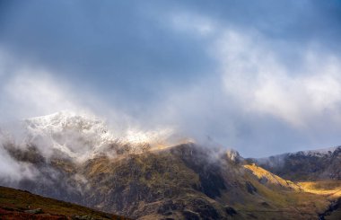 Cwm Idwal 'daki karla kaplı Glyderau tepelerinde bir sis girdabı otluyor ve antik Galler yamaçlarında değişen güneş ışığı ceplerini ortaya çıkarıyor.