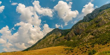 Arnavutluk 'un Prespa bölgesindeki gizli mağaraların delik deşik ettiği, bulutlarla dağılmış bir yaz gökyüzü altında, altın çayır ve kekik kokulu tepeler tırtıklı kireçtaşı kayalıklarına yükseliyor.