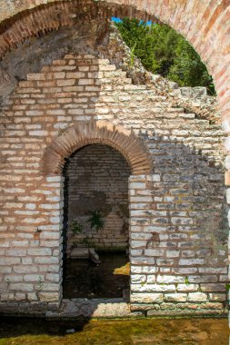 Arnavutluk 'un güneyindeki Butrint arkeolojik harabeleri içindeki yansıtıcı bir su kanalının kenarında antik kireçtaşı kemerli güneş ışığı