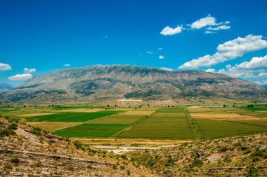 Nemercka 'nın kireçtaşı tepelerinin panoramik süpürgesi yama arazisi üzerinde yükseliyor ve bulut noktalı Arnavut gökyüzünün altında dolambaçlı bir vadi yolu