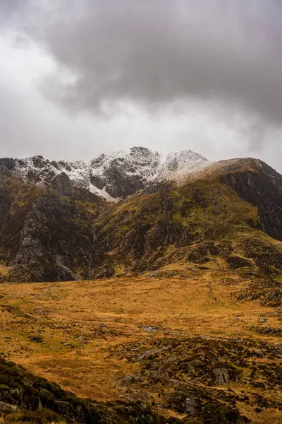 Kara kara düşünen bulutlu gökyüzü, Cwm Idwal 'ın buzul zirvelerini altın dişli ve engebeli yamaçlarla taçlandırıyor.