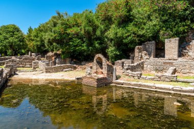 Arnavutluk 'un Butrint Ulusal Parkı' ndaki güneşli Roma hamamı, alg dolu yansıtma havuzu ve yemyeşil orman zeminiyle harabeye döndü