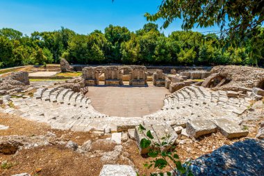 Arnavutluk 'un Butrint Ulusal Parkı' ndaki antik Roma tiyatrosu harabeleri, yeşil Akdeniz ormanlarının ortasında katmanlanmış taş koltuklar ve ahşap sahnelerle dolu
