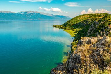 Arnavutluk 'un Lin kentinde geniş bir gök kubbeli gökyüzünün altındaki Ohri Gölü üzerindeki kireçtaşı çıkıntısı altında zümrüt kıyı şeridi kıvrımları oluştu