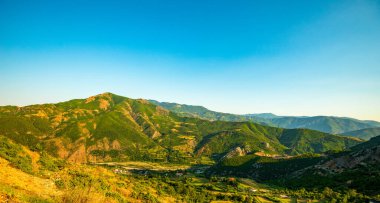 Rruga Egnatia 'nın panoramik manzarası (Via Egnatia) açık bir gök mavisi Arnavut gökyüzü altında yeşil dağ vadileri ve teraslı tarım arazileri arasında dönüyor