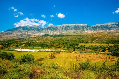 Gezinen turkuaz Vjosa Nehri Permet yakınlarındaki engebeli Arnavut dağlarının altındaki alüvyonlu ovalarda örülmüş kanallar kazıyor