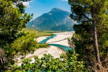 Vjosa Nehri 'nin zümrüt kurdelesi, güneşte parlayan çakıl taşları ve Arnavut gökyüzünün altındaki çam ağacından yapılmış kireç taşı tepelerinden geçiyor
