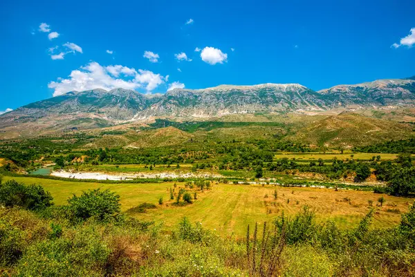 Gezinen turkuaz Vjosa Nehri Permet yakınlarındaki engebeli Arnavut dağlarının altındaki alüvyonlu ovalarda örülmüş kanallar kazıyor