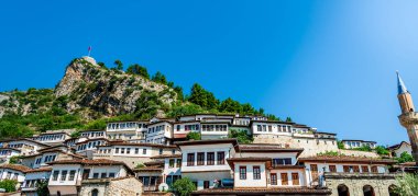Berat 'ın Osmanlı döneminden kalma, Arnavutluk' taki Berat Kalesi 'nin kayalıklarının altında canlı bir yaz gökyüzü altında kümelenmiş, beyazlatılmış tepe evleri var.