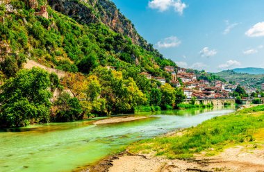 Berat 'ın güneş lekeli Osmanlı beyazlatılmış evleri kireçtaşı yamaçlarda katmanlıydı. Zümrüt renkli Osum Nehri' ne bakan parlak mavi gökyüzünün altında.