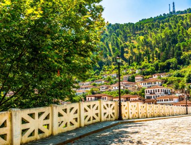 Berat 'ın beyaz boyalı Osmanlı evleri Gorica Köprüsü' nden canlı bir yaz gökyüzünün altında Osum Nehri boyunca uzanan kireçtaşı yamaçlarından aşağı dökülüyor.