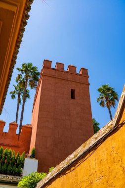 Terracotta surları kulesi ve çentikler açık Sevilla gökyüzünün altında sallanan palmiyeler ve toprak duvarlar tarafından çerçevelenmiş.