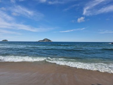 Bulutlu mavi gökyüzü ve mavi su kumlu güzel plaj ve arka planda küçük bir ada. 