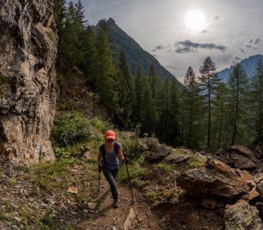 Kayalık patika dağları, orman ve dramatik gökyüzü manzaralı bir yürüyüşçü. İtalya