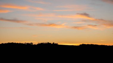 Gün batımında parlayan sakin manzara. Canlı bulutlar. Karanlık ağaç tepesi siluetleri.