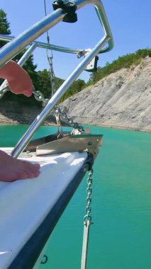 Lowering anchor sailboat into turquoise Lake Serre-Poncon rocky shores