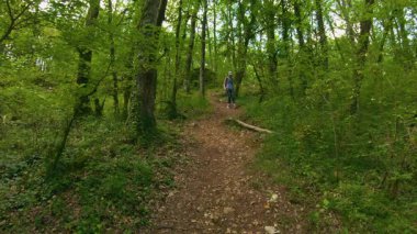 Kadın dikkatli bir şekilde orman yolunda yürüyor yoğun yeşil yapraklar.