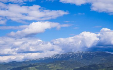 Uçsuz bucaksız bir dağ silsilesinin nefes kesici panoramik manzarası. Mavi dramatik bir gökyüzü altında kar kaplı tepeler ve tüylü beyaz bulutlar. Mükemmel bir özgeçmiş..