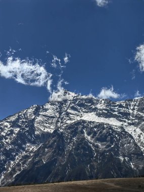 Karla kaplı dağ yolu, temiz hava ve yeşil otlarla dolu doğa manzarası.