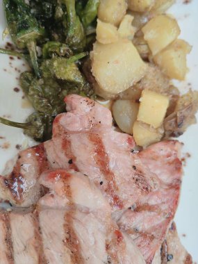 Baharatlı salamurada pişirilmiş leziz tavada domuz pirzolası ve biberiyeyle süslenmiş haşlanmış bebek patatesleriyle servis edilmiş..