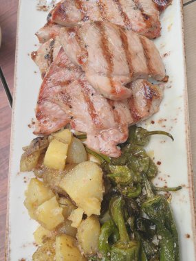 Baharatlı salamurada pişirilmiş leziz tavada domuz pirzolası ve biberiyeyle süslenmiş haşlanmış bebek patatesleriyle servis edilmiş..