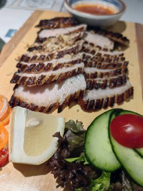 Soslu kızarmış domuz filetosu, taze kekik, yeşillik ve ahşap masada kiraz domatesleri.