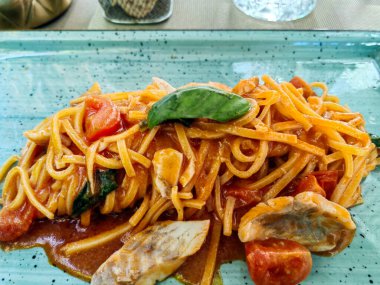 Domates kirazlı spagetti deniz ürünleri. Modern tabakla servis edilen fesleğenle süslenmiş domates soslu spagetti.