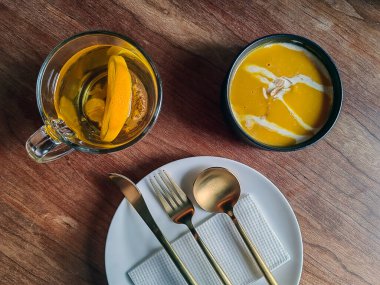 Krema desenli baharatlı baharatlı ve kızarmış balkabağı kremalı çorba. Çatal bıçakla beyaz sofra takımında servis edilir..