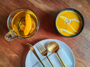 Krema desenli baharatlı baharatlı ve kızarmış balkabağı kremalı çorba. Çatal bıçakla beyaz sofra takımında servis edilir..