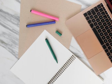 Evde çalışmak, dizüstü bilgisayarlı masa yaratıcı ofisi, boş not defteri, not defteri ve renkli bir kalem..