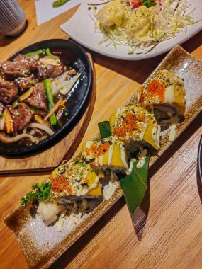 Çeşitli suşi tabakları, sashimi ve nigiri hafif ahşap masalı bir Japon restoranında.