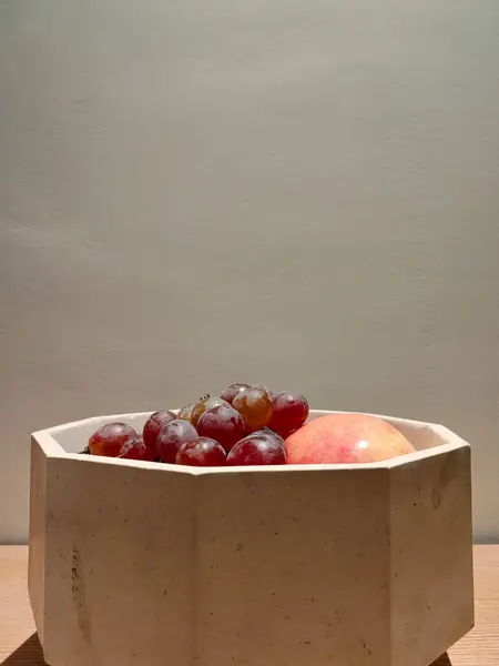 Üzüm ve elma bej bir tencerede dekoratif gri duvar arka planına karşı.