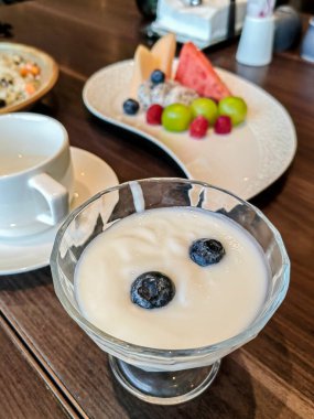 Üstünde yaban mersini ve meyve salatası olan bir fincan peynirli kek..