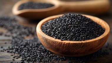 Köy ahşap bir kâseye istiflenmiş siyah susam tohumlarının yakın plan görüntüsü. Ek tohumlar da koyu ahşap bir yüzeye saçılmış. Bileşim dokuyu, doğal tonları ve organik basitliği vurgular.
