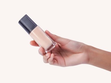 Elinde beyaz arka planda izole edilmiş siyah kapaklı bir bej fondöten şişesi var..