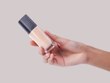 Elinde siyah şapkalı bir bardak bej fondöten var. Güzellik teması için ideal.