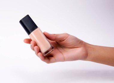 Elinde beyaz arka planda izole edilmiş siyah kapaklı bir bej fondöten şişesi var.