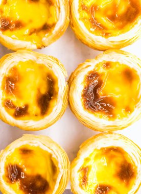 Sarı ve kahverengi renkte bir tabak hamur işi yakın plan. Pastel de nata. Hamur işleri sıraya dizildi ve küçük ve tatlı görünüyor.