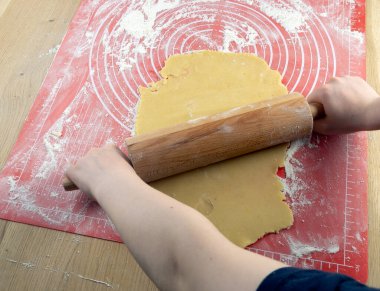Bir kişi hamuru kırmızı bir hasırın üzerine yuvarlıyor. Hamur altın sarısı ve o pişirmeye hazır. Kişi hamuru yassılaştırmak için merdane kullanıyor ve hamuru hasırın üzerine yayılıyor.