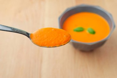 Bir kaşık çorba bir kase çorbaya karşı bekletiliyor. Kaşık gümüş, kase de seramik.