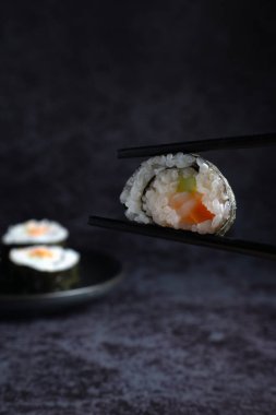 Bir parça suşi ön planda çubuklarla gösteriliyor. Suşi ikiye bölündü. Pirinç, sebze gibi çeşitli malzemeler ortaya çıktı..