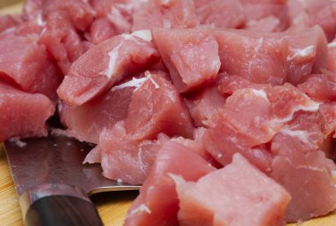 Detaylı bir yakın plan, küçük küplere kesilmiş çiğ domuz eti yığınını ve biraz da yağ misketi gösteriyor. Bıçak sol altta kısmen görülebilir.